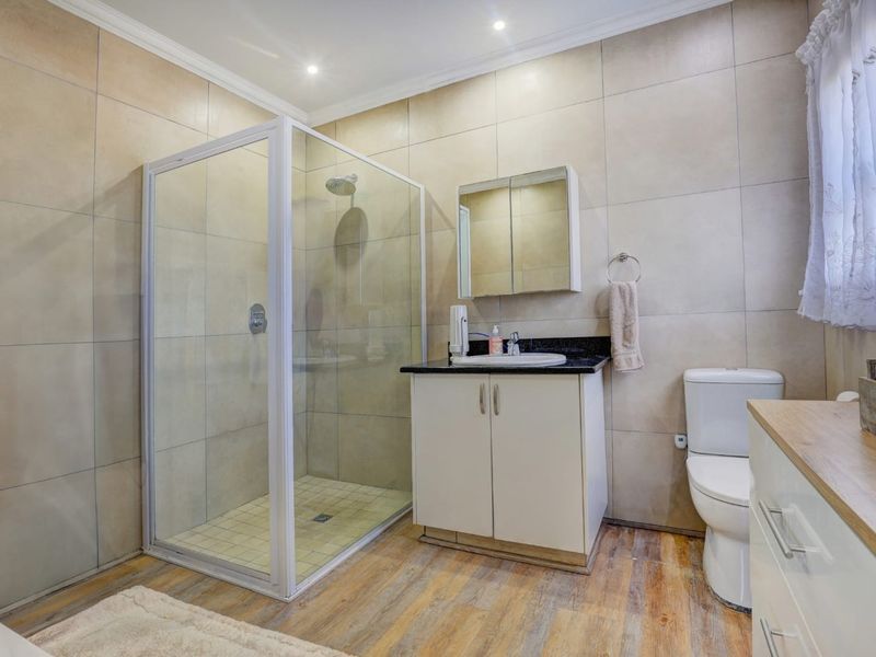 Modern bathroom featuring a glass shower enclosure, vanity with granite countertop, medicine cabinet, and neutral wall tiling.