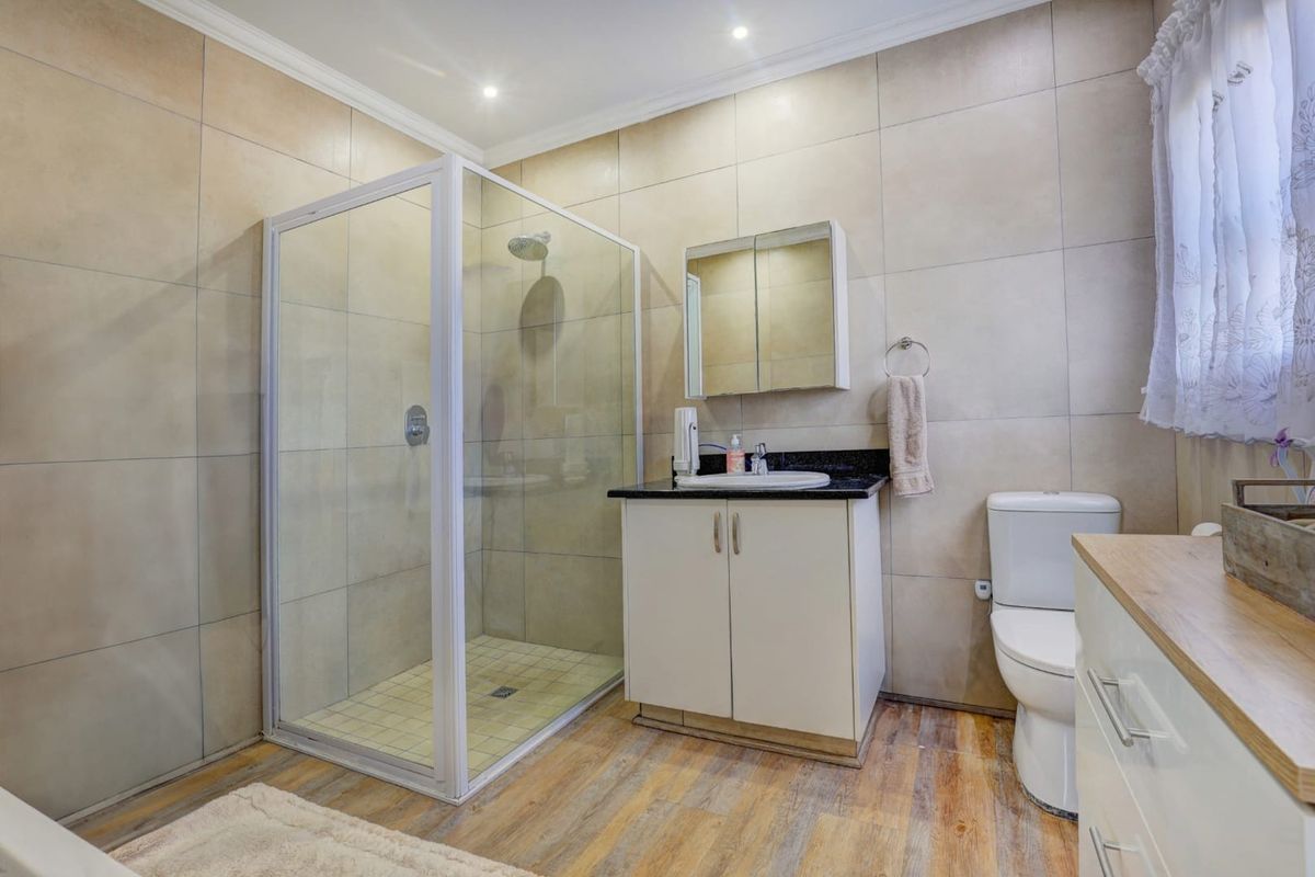 Modern bathroom featuring a glass shower enclosure, vanity with granite countertop, medicine cabinet, and neutral wall tiling.