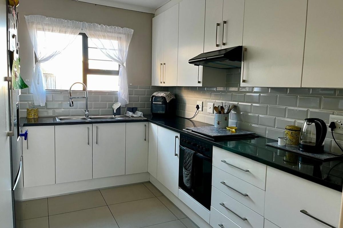 Modern kitchen featuring white cabinetry, contrasting black granite countertops, subway tile backsplash, and integrated stainless steel appliances.