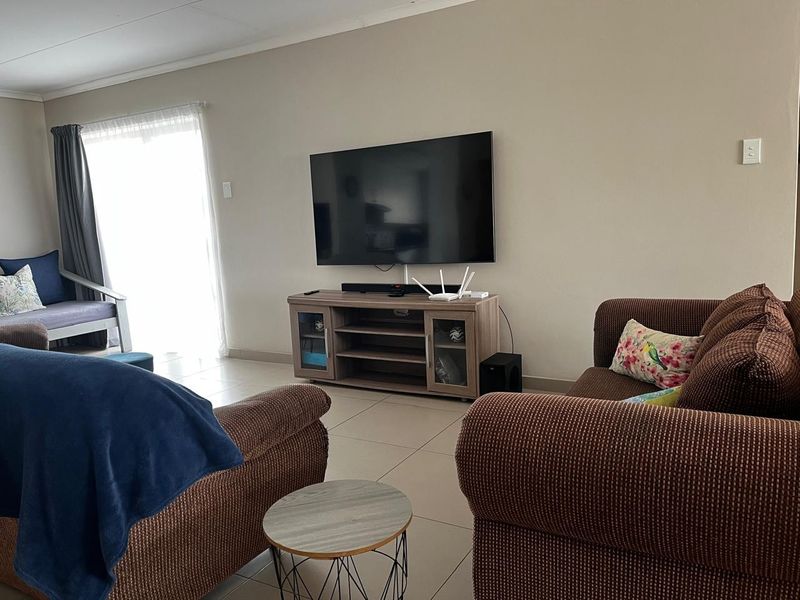 A comfortable living room featuring neutral wall tones, tiled flooring, and a sliding glass door providing natural light.