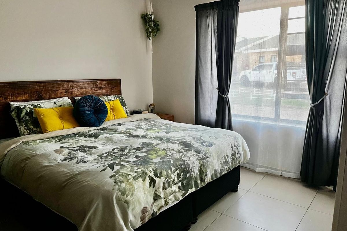 A well-lit bedroom featuring neutral wall tones, tiled flooring, and a large window allowing for natural light.