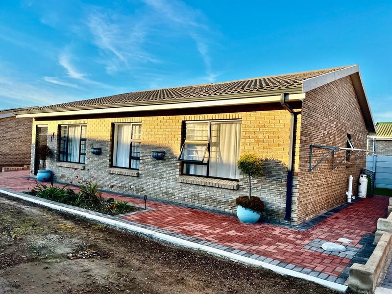 A well-maintained single-story brick house featuring a tiled roof, aluminium window frames, and a neat paved walkway along the rear exterior.