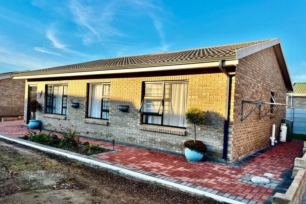 A well-maintained single-story brick house featuring a tiled roof, aluminium window frames, and a neat paved walkway along the rear exterior.