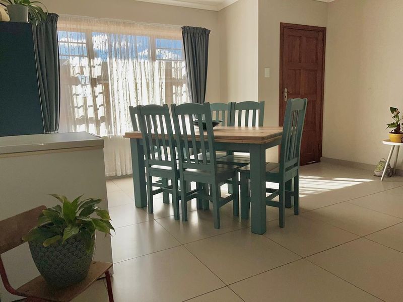 A bright dining area featuring neutral tiled flooring, a large window allowing natural light, and a solid timber door.