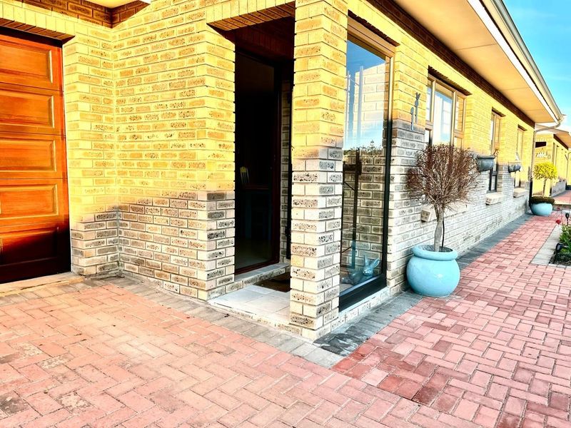 A well-maintained face brick exterior featuring a paved entrance area, timber front door, and large glass windows providing natural light.