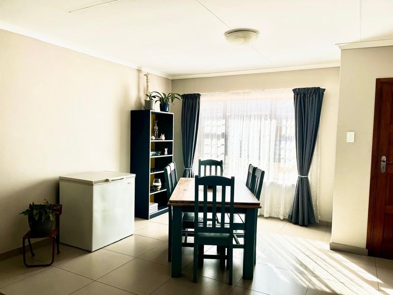 A bright dining room featuring neutral wall tones, tiled flooring, and a large window allowing for ample natural light.
