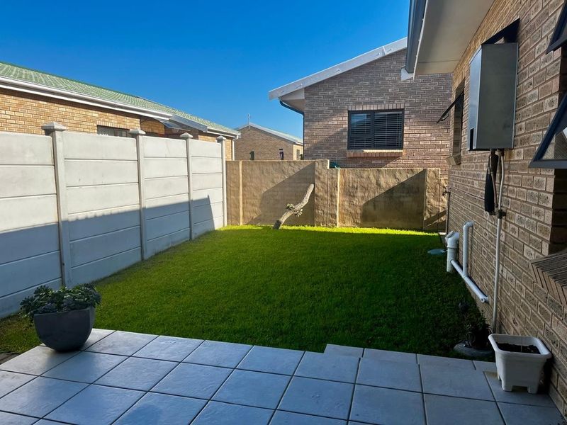 A private rear garden featuring a tiled patio area, a small lawn, and secure boundary walling.