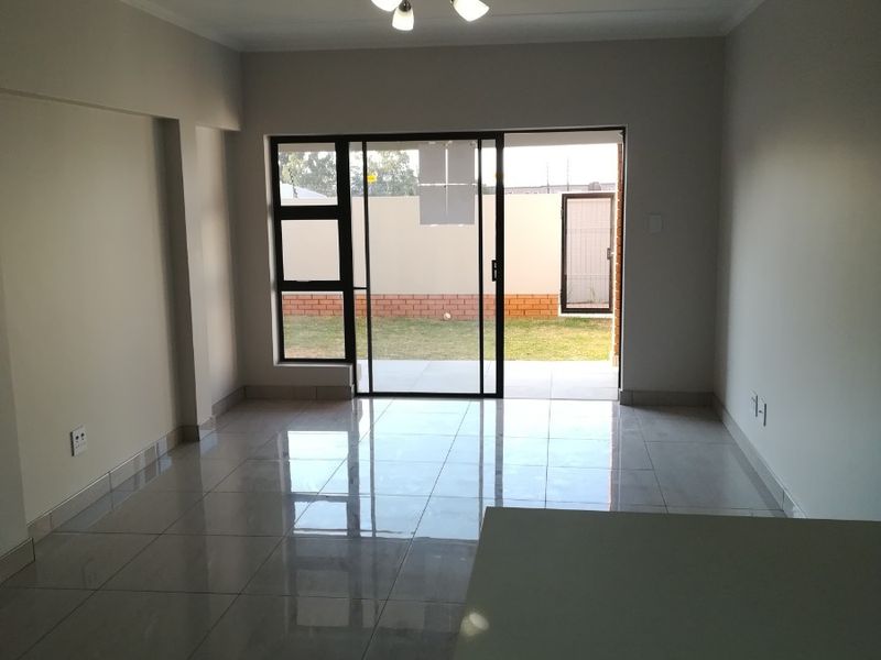 An open-plan living area featuring polished tiled floors, modern ceiling lighting, and a sliding glass door providing direct access to the rear garden.