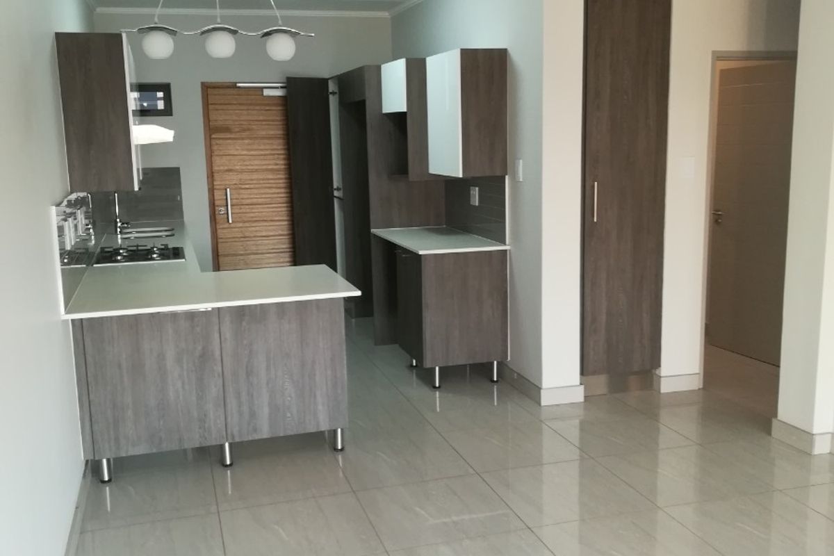 Modern kitchen featuring sleek dark wood cabinetry, stone countertops, a gas hob, and polished tiled flooring in an open-plan layout.