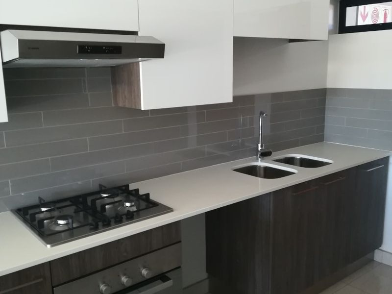Modern kitchen featuring sleek white and dark wood cabinetry, quartz countertops, a gas hob, built-in oven, and a stylish grey tiled backsplash.