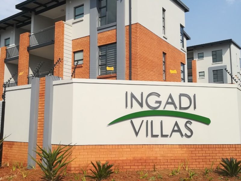Front entrance view of Ingadi Villas townhouse complex featuring modern brick and plaster facade, balconies, and secure perimeter fencing.