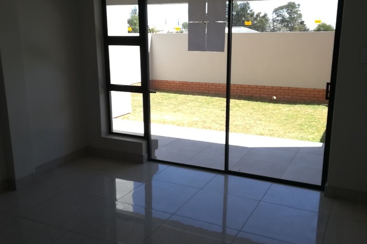An empty living room featuring large sliding glass doors that open onto a private garden area with tiled flooring throughout.