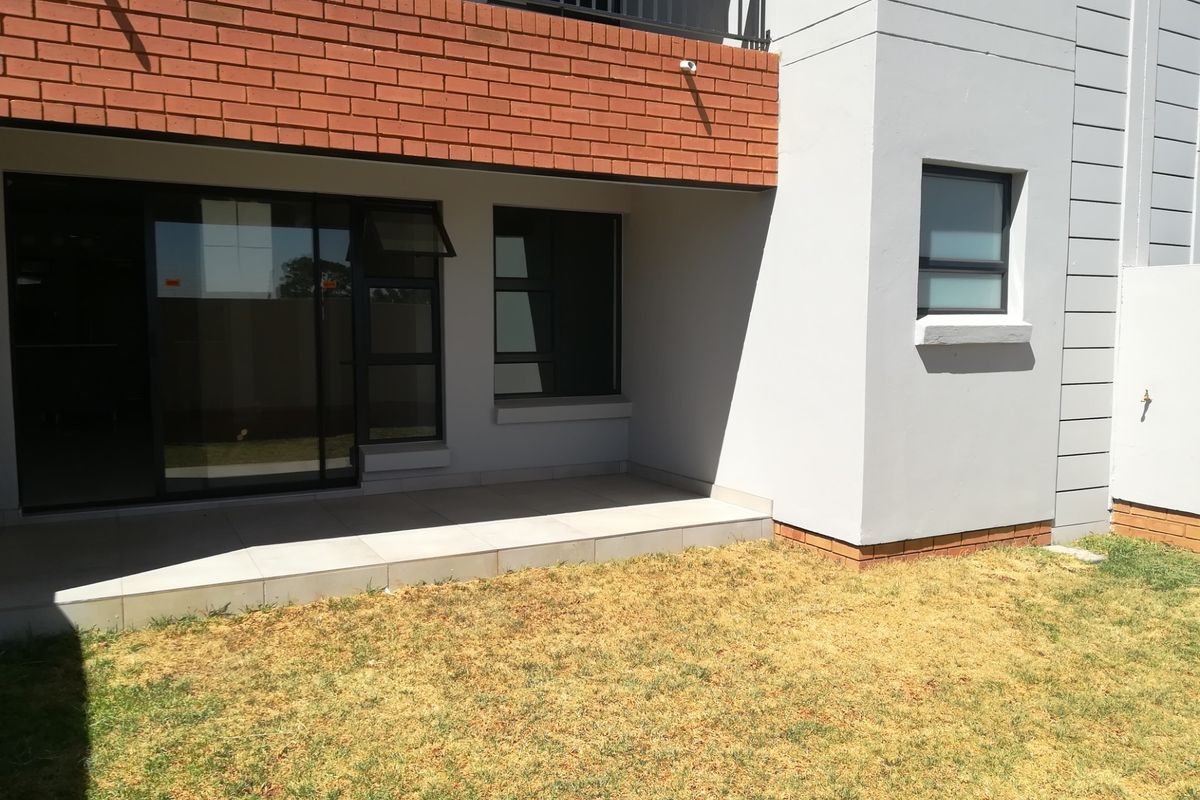 Rear view of the townhouse featuring a tiled patio, sliding glass doors, and a small private garden area with brick and plaster finishes.