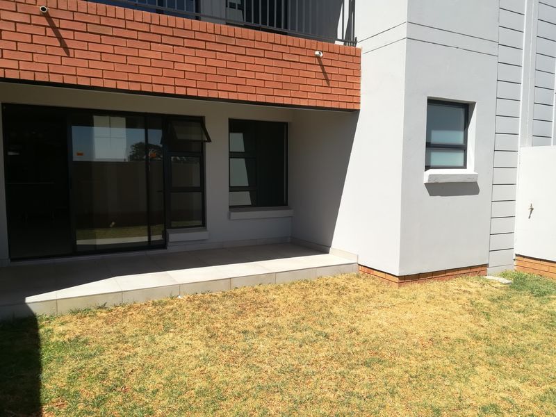 Rear view of the townhouse featuring a tiled patio, sliding glass doors, and a small private garden area with brick and plaster finishes.