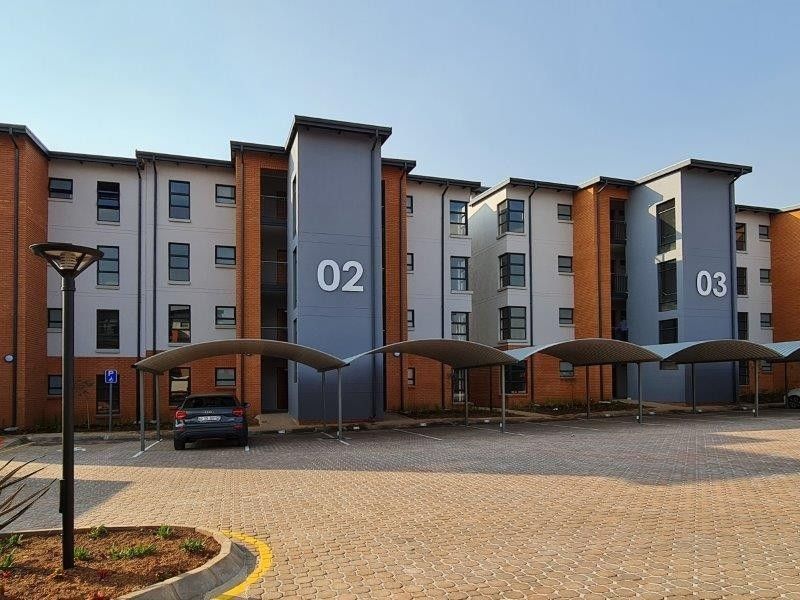 Front view of a modern townhouse complex featuring multi-story residential blocks, paved parking areas, and covered carports.