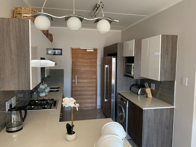 Modern kitchen featuring sleek wood-grain and white cabinetry, stone countertops, gas hob, built-in appliances, and contemporary pendant lighting.