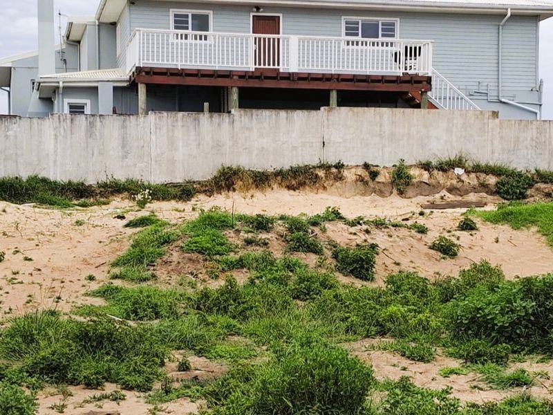Rear view of a residential property featuring a raised timber deck, concrete boundary wall, and an undeveloped sandy garden area.