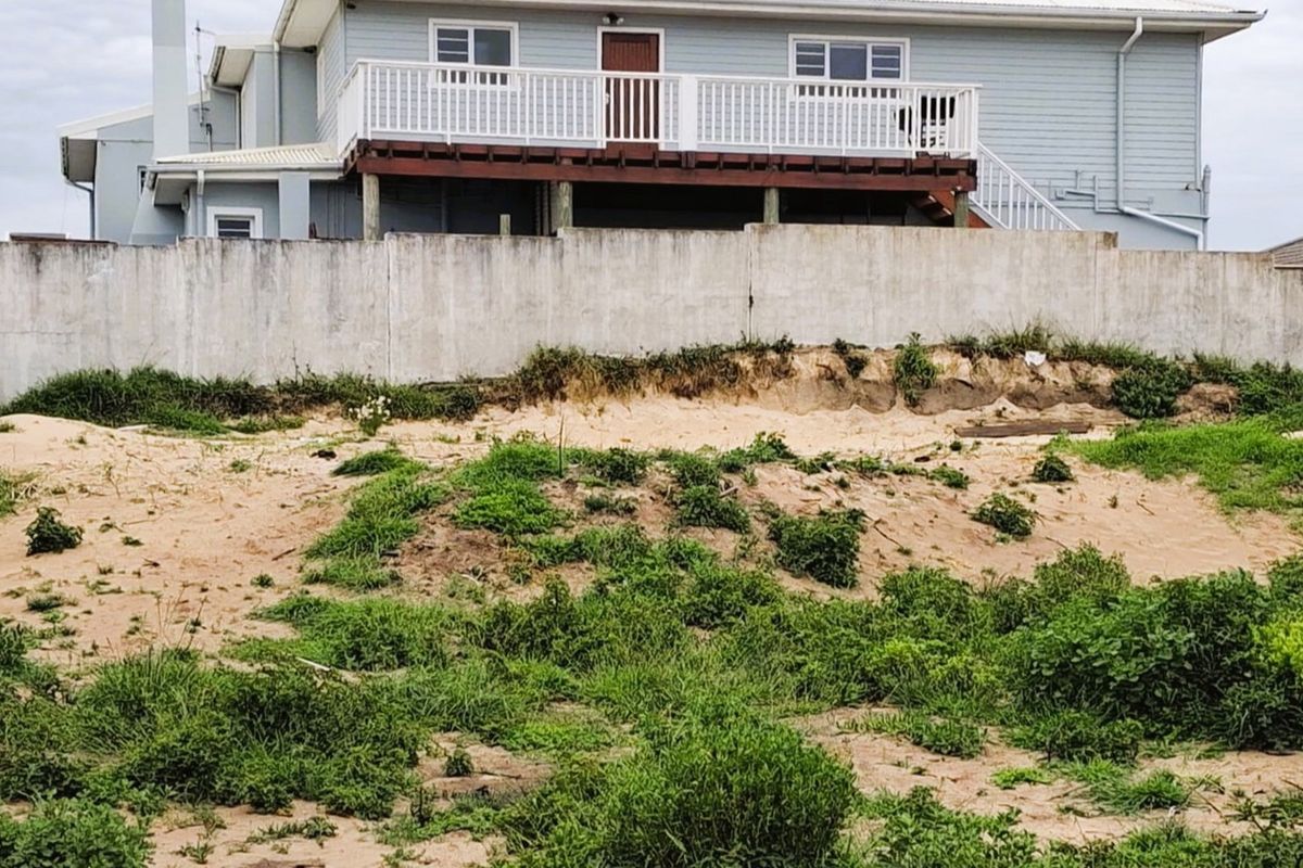Rear view of a residential property featuring a raised timber deck, concrete boundary wall, and an undeveloped sandy garden area.