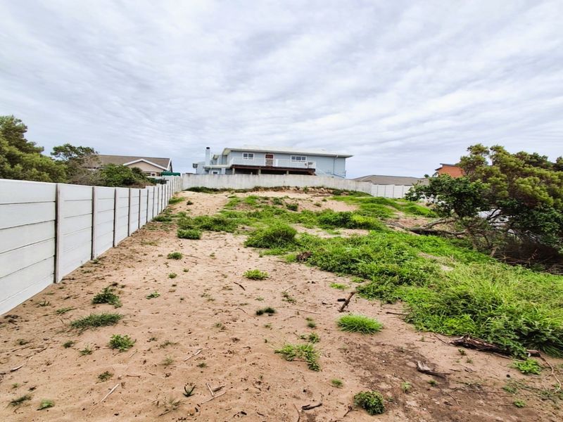A vacant residential plot featuring a precast concrete boundary wall and sloped, sandy terrain with natural vegetation.