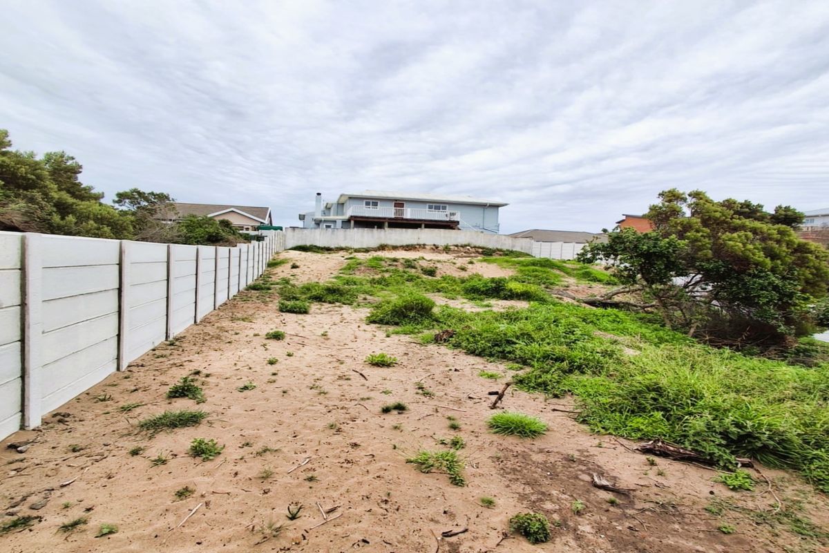A vacant residential plot featuring a precast concrete boundary wall and sloped, sandy terrain with natural vegetation.