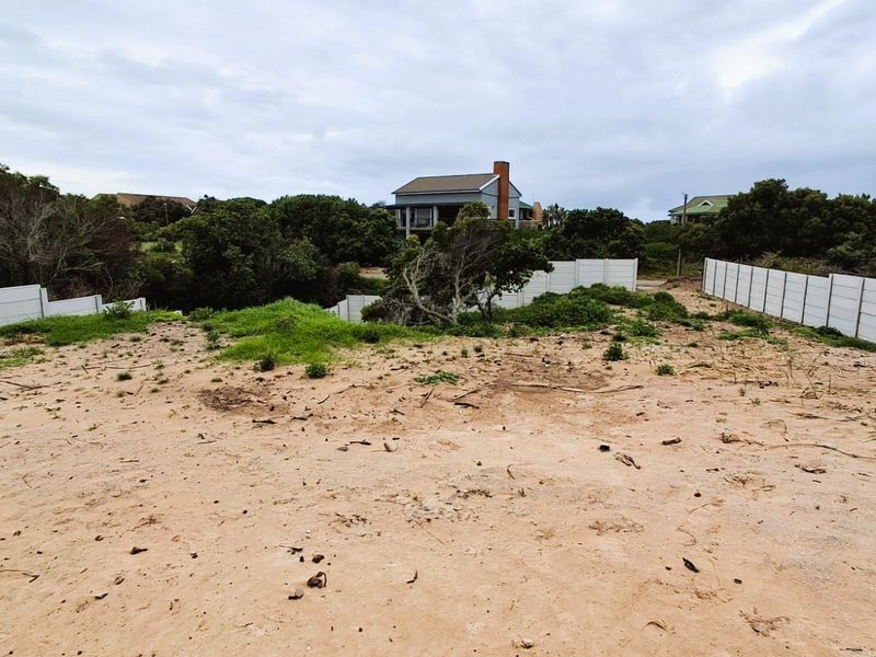A vacant residential plot featuring sandy terrain, established indigenous vegetation, and enclosed by precast concrete boundary walls.