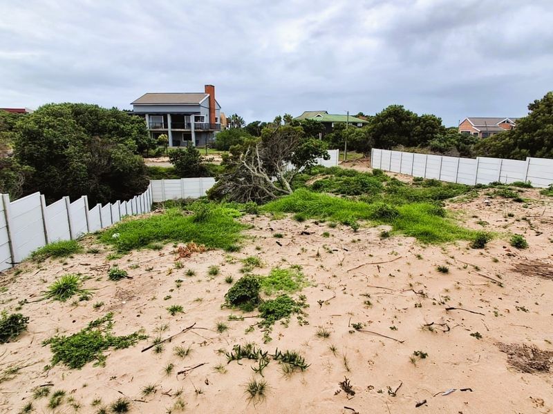 A vacant residential plot featuring sandy terrain and established precast concrete boundary walls, situated in a coastal neighborhood setting.