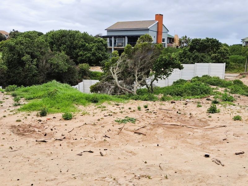 A vacant residential plot featuring sandy terrain, natural vegetation, and precast concrete boundary walls, offering a clear view of the surrounding neighborhood.
