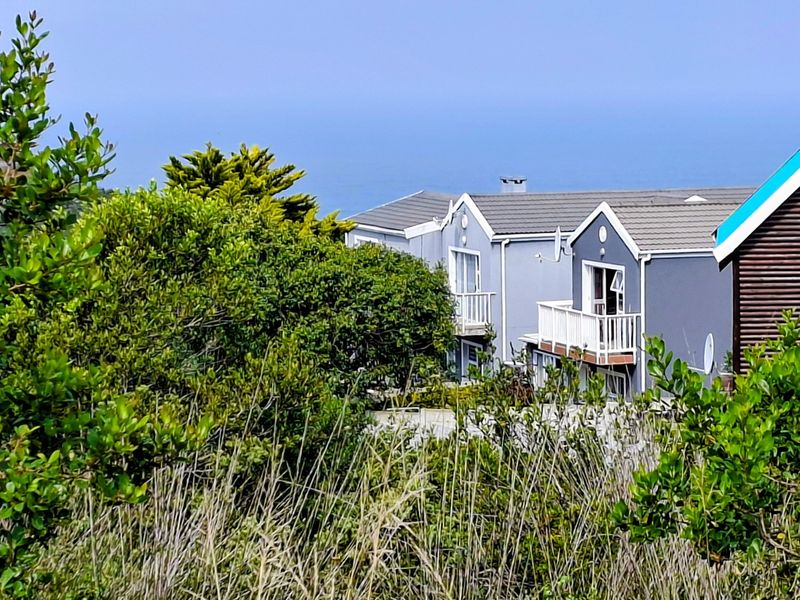 A view of the rear elevation of the duet property, featuring tiled roofing, balconies, and sliding door access, set against a coastal backdrop.