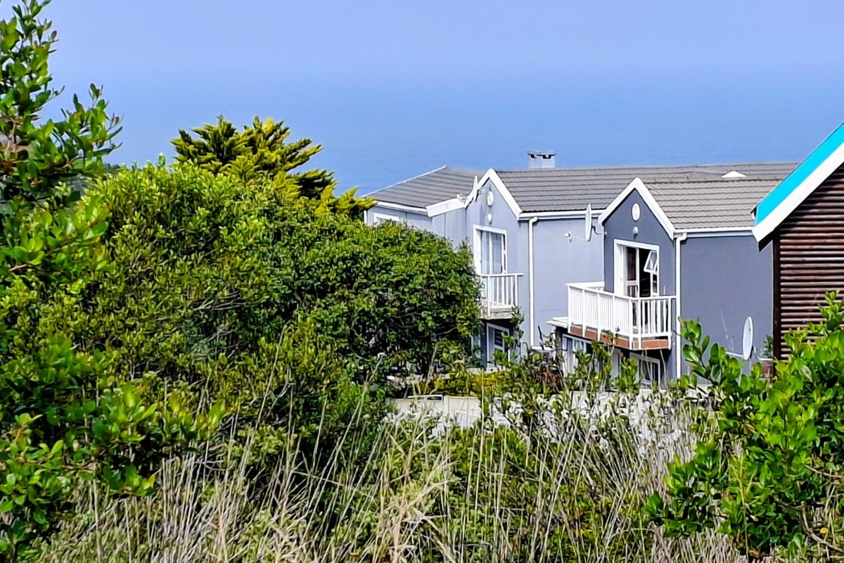 A view of the rear elevation of the duet property, featuring tiled roofing, balconies, and sliding door access, set against a coastal backdrop.