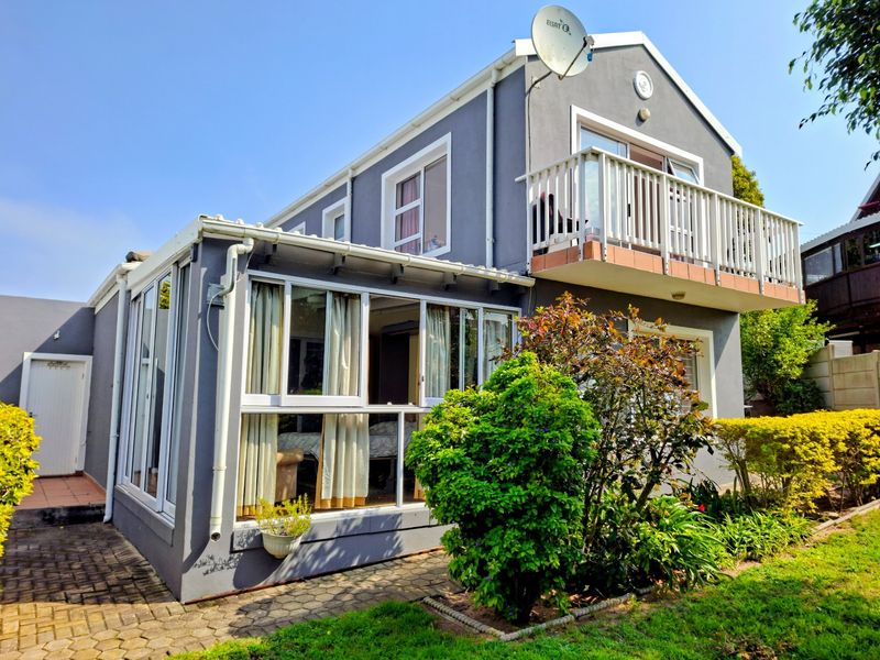 Rear view of a two-story duet property featuring a balcony, enclosed sunroom, and paved garden area.