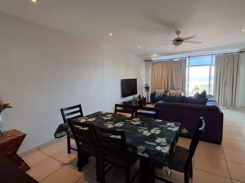 An open-plan living and dining area featuring tiled flooring, recessed lighting, a ceiling fan, and direct access to a balcony with ocean views.