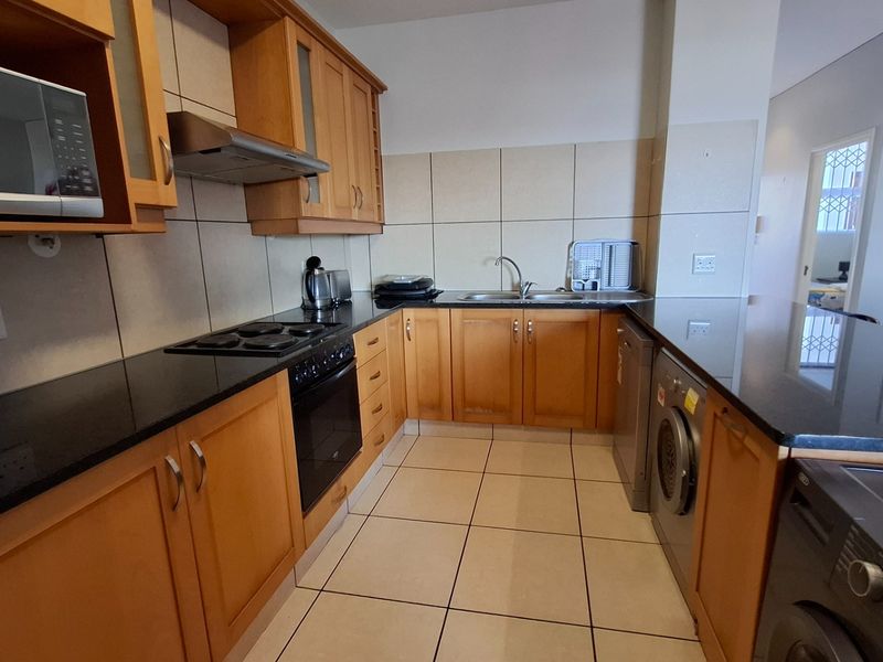 Functional kitchen featuring wooden cabinetry, black granite countertops, integrated appliances, and tiled finishes, offering a practical layout for daily cooking and preparation.