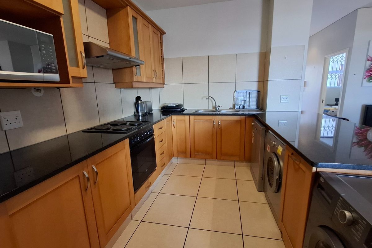 Functional kitchen featuring wooden cabinetry, black granite countertops, integrated appliances, and tiled finishes, offering a practical layout for daily cooking and preparation.
