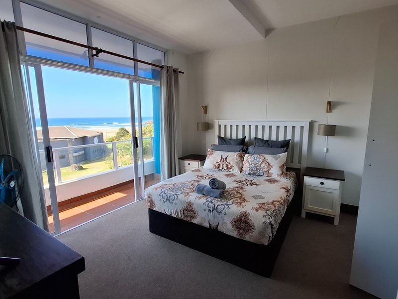 A bright bedroom featuring carpeted flooring and a large sliding glass door that opens onto a balcony with scenic ocean views.