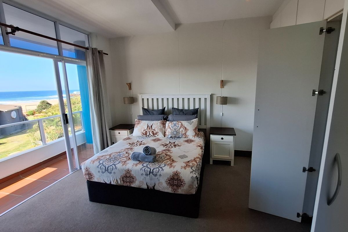A bright bedroom featuring carpet flooring, built-in wardrobes, and a large sliding glass door providing access to a balcony with ocean views.