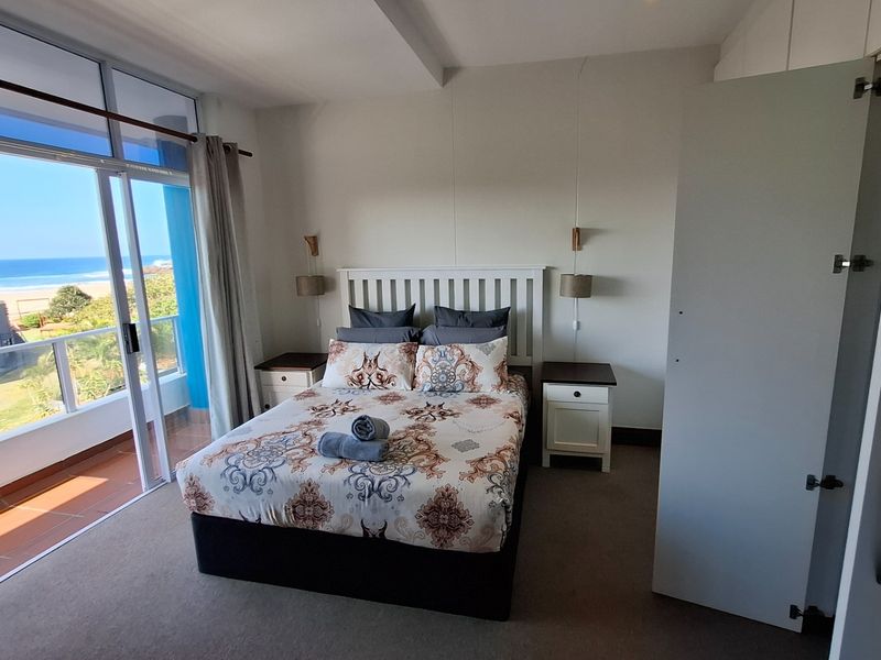 A bright bedroom featuring carpet flooring, built-in wardrobes, and a large sliding glass door providing access to a balcony with ocean views.