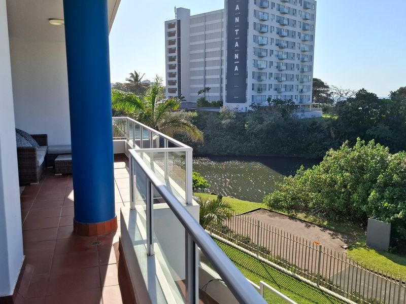 A spacious balcony featuring tiled flooring, a modern glass balustrade, and a structural column, offering scenic views of the surrounding area and river.