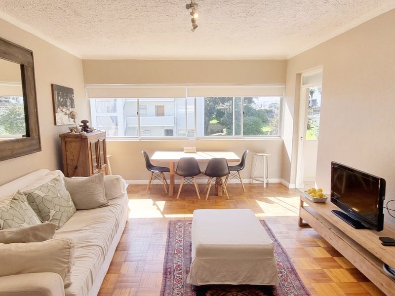 A bright living room featuring classic parquet flooring, large windows providing natural light, and a textured ceiling finish.