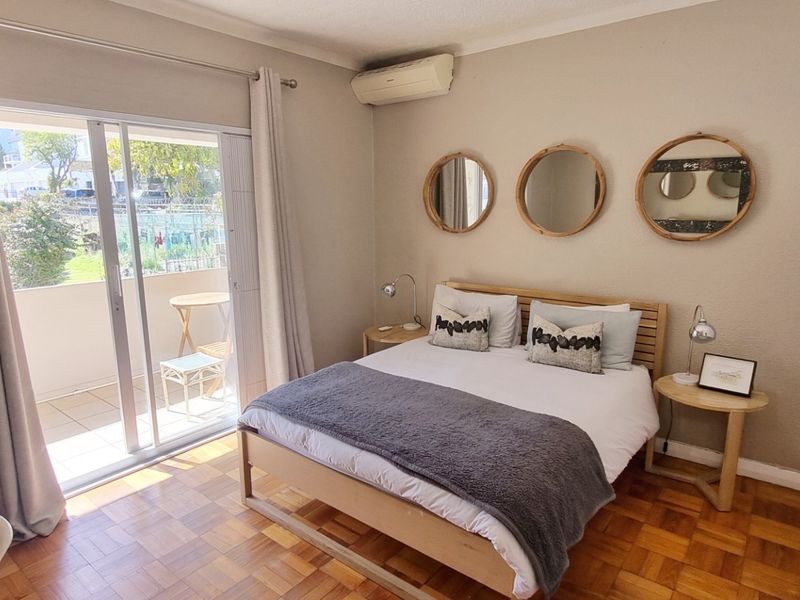 A well-maintained bedroom featuring classic parquet flooring, a built-in wardrobe, wall-mounted air conditioning, and direct access to a private balcony through sliding glass doors.