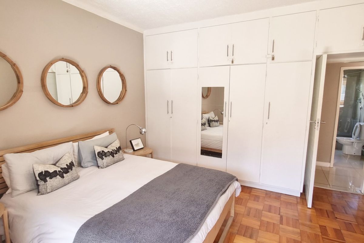 A well-maintained bedroom featuring classic parquet flooring and extensive floor-to-ceiling built-in cupboards, with an adjoining en-suite bathroom visible.