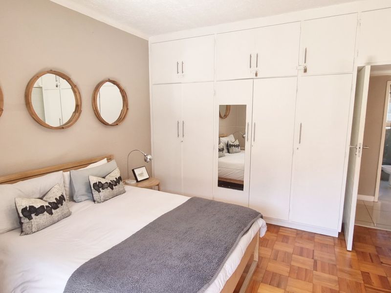 A well-maintained bedroom featuring classic parquet flooring and extensive floor-to-ceiling built-in cupboards, with an adjoining en-suite bathroom visible.