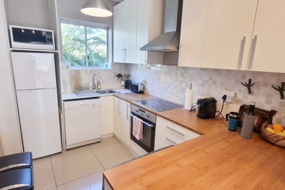 A functional kitchen featuring wooden countertops, tiled backsplash, built-in oven, electric hob, extractor fan, and integrated dishwasher with ample cabinet storage.