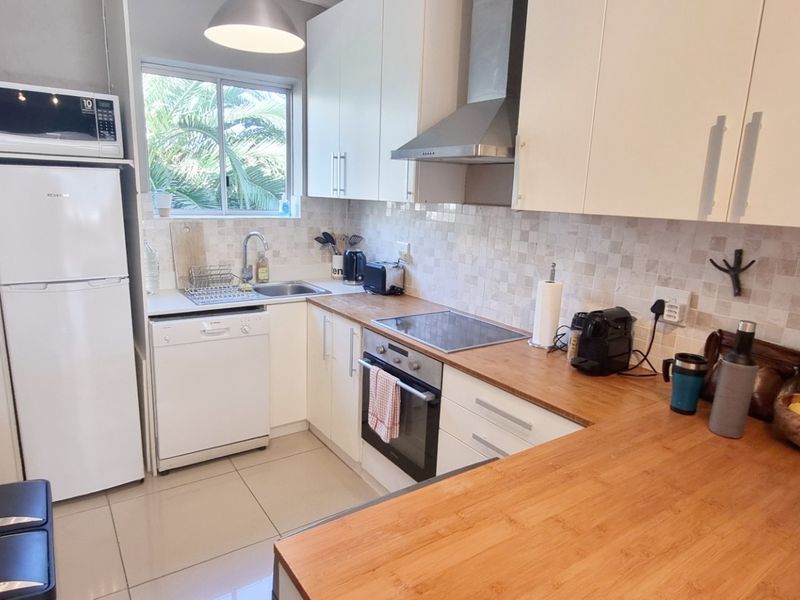 A functional kitchen featuring wooden countertops, tiled backsplash, built-in oven, electric hob, extractor fan, and integrated dishwasher with ample cabinet storage.
