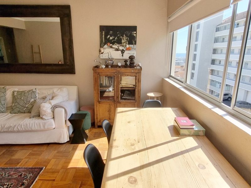 A bright living area featuring classic parquet flooring and a large window with natural light, offering an urban outlook.