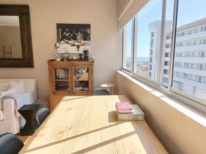A bright living area featuring large sliding windows that provide natural light and views, complemented by classic parquet flooring.