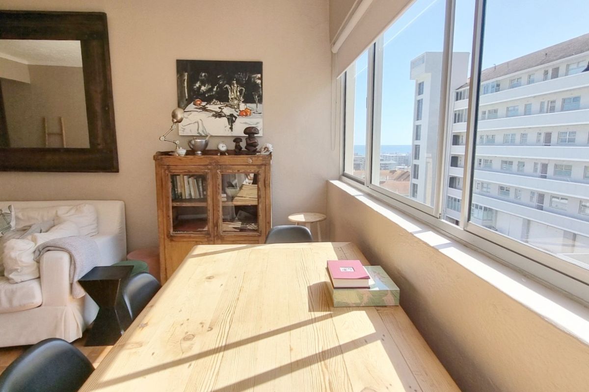 A bright living area featuring large sliding windows that provide natural light and views, complemented by classic parquet flooring.
