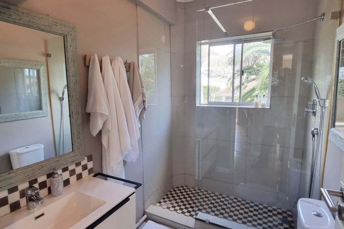 A well-maintained bathroom featuring a modern vanity, a glass-enclosed shower with checkered tile accents, and a toilet.