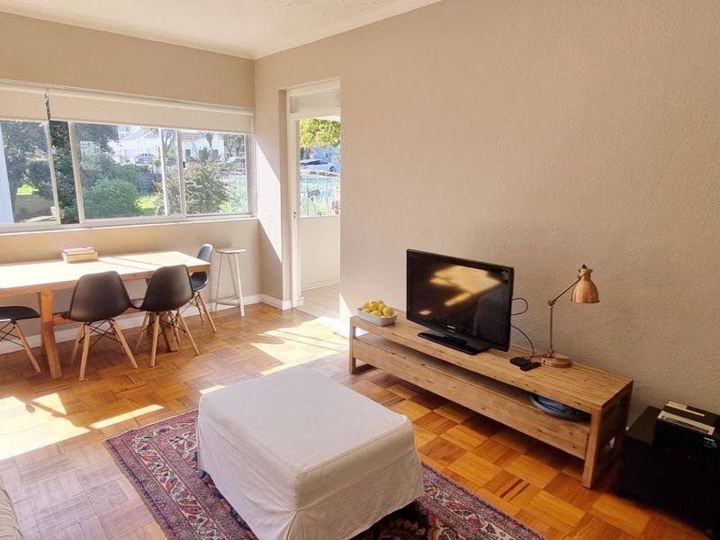 Bright open-plan living and dining area featuring classic parquet flooring, large windows providing natural light, and direct access to an outdoor balcony.