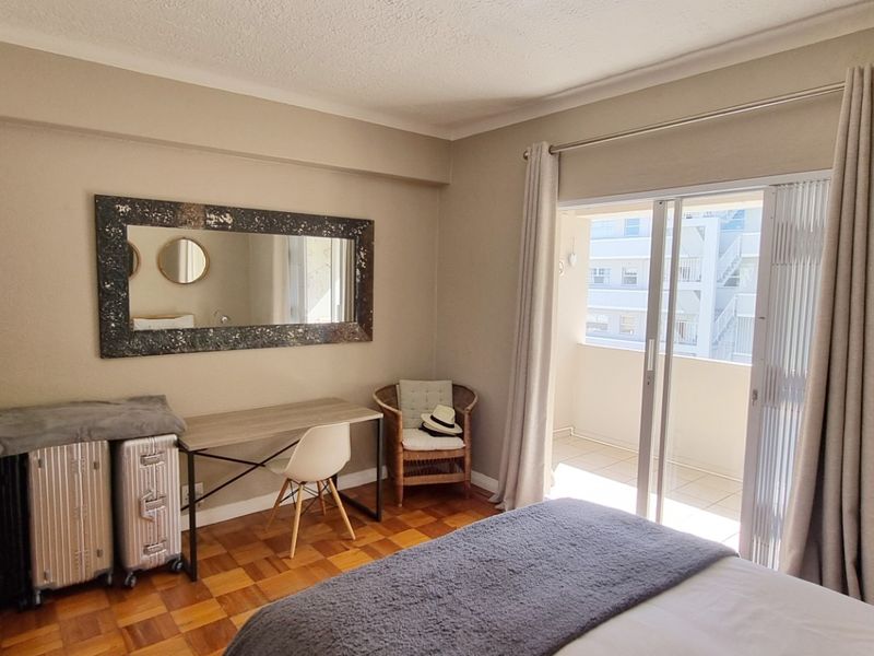 A bedroom featuring parquet flooring, built-in cupboards, and a sliding glass door providing direct access to a private balcony.