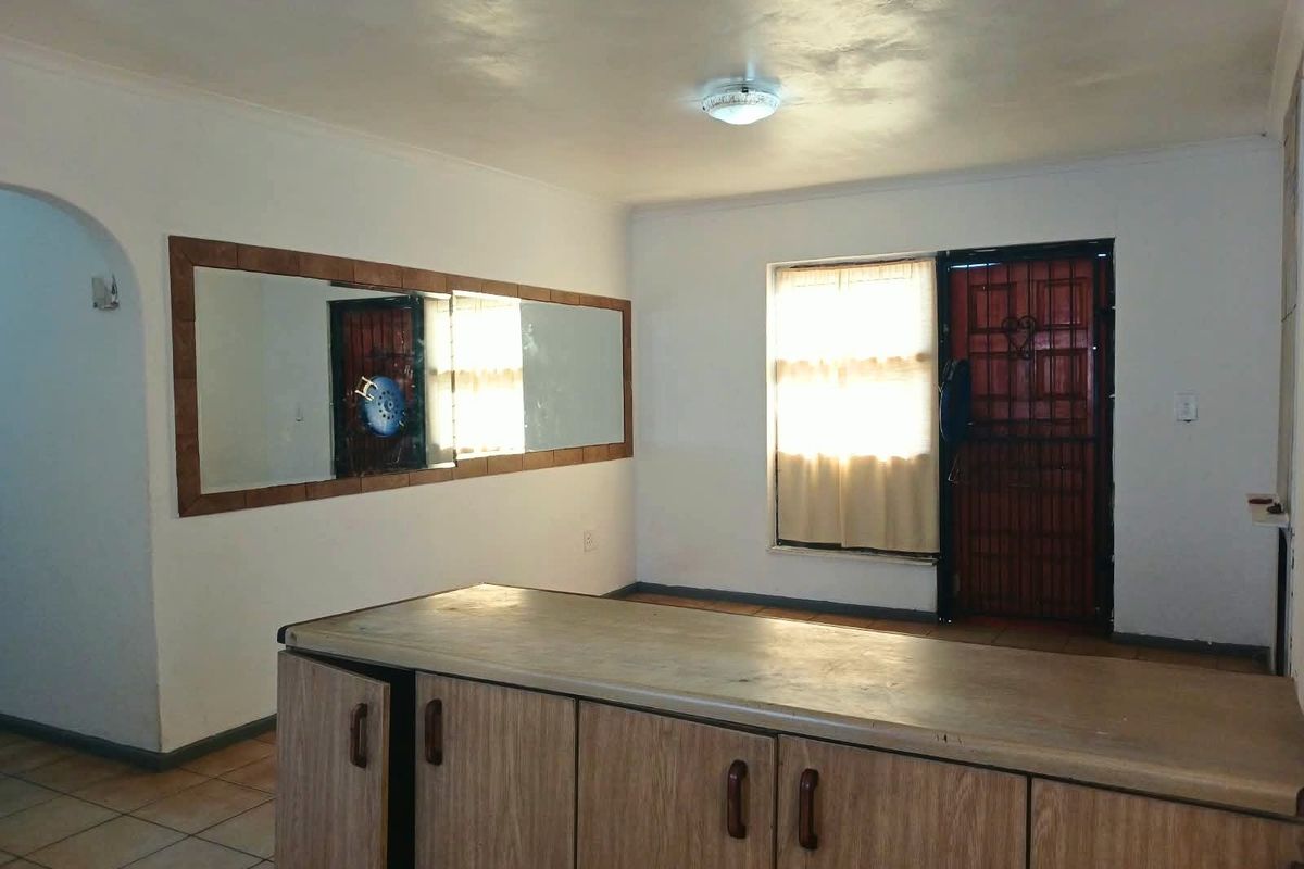 A functional kitchen area featuring built-in cabinetry, tiled flooring, and a security gate, offering a blank canvas for potential renovation and modernization.